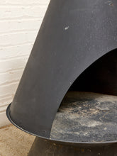 Load image into Gallery viewer, Close-up of a black metal fireplace insert or stove component with a curved opening, showing a dusty interior and a white painted brick wall in the background.
