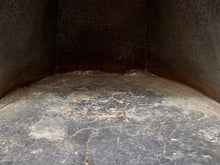 Load image into Gallery viewer, Close-up of the inside corner of a dark metal fireplace or stove chamber with a worn, dusty gray floor and rusted metal walls.
