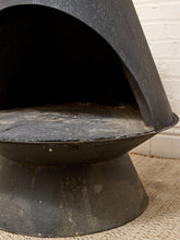 Load image into Gallery viewer, A close-up of a black metal outdoor patio chair with a wide base and curved back, positioned on a textured beige rug against a white brick wall.
