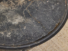 Load image into Gallery viewer, A close-up of a heavily worn, cracked black circular surface, likely a vintage stool or table top, showing significant scuffing and wear, with a beige woven fabric surface visible underneath at the edge.
