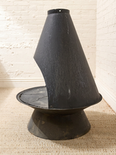 Load image into Gallery viewer, A black metal cone-shaped fireplace chimney guard or damper assembly mounted on a circular base, set on a beige carpet against a white brick wall.

