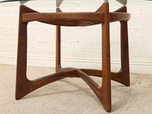 Load image into Gallery viewer, A mid-century modern wooden table base or stool with a rich dark brown walnut finish, featuring curved legs and a central support beam, set against a white brick wall and light beige carpet.
