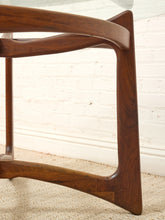 Load image into Gallery viewer, Close-up of a mid-century modern wooden chair leg with a rich walnut finish, set against a white brick wall and beige carpet.

