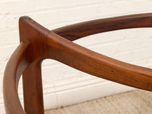 Load image into Gallery viewer, Close-up of a wooden chair frame with curved armrests and a polished medium-brown finish, set against a white brick wall and light carpet.
