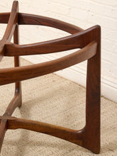 Load image into Gallery viewer, A close-up of a mid-century modern wooden chair base, featuring a warm dark brown walnut finish, set on a beige woven rug against a white brick wall.
