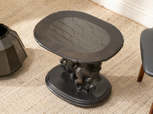 Load image into Gallery viewer, A dark carved wooden side table with an oval top and lion pedestal base, shown on a woven beige rug.
