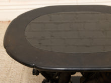 Load image into Gallery viewer, Close-up of a dark oval table top with a glossy finish, showing a small visible crack along the edge, set against a light beige carpet and white wall background.
