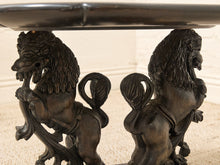 Load image into Gallery viewer, Close-up of a dark carved table base featuring two lion figures supporting the structure, photographed indoors against a light neutral wall and carpet.
