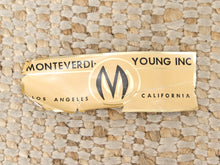 Load image into Gallery viewer, A torn gold-colored paper label with black text reading 'MONTEVERDI YOUNG INC' and a large 'M' logo, placed on a woven beige rug.
