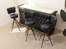 Load image into Gallery viewer, Vintage black upholstered bar with deep button tufting and brass-tone trim paired with three black swivel bar stools on metal bases
