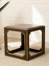 Load image into Gallery viewer, A dark brown wooden cube side table with gold-painted trim and open lattice panels, set on a beige carpet against a white brick wall.
