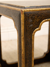 Load image into Gallery viewer, Close-up of an antique-style wooden table corner showing a dark brown and black textured lacquer finish with prominent gold gilded trim.
