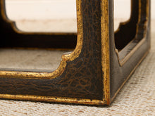 Load image into Gallery viewer, Close-up detail of a dark wood furniture leg corner with a glossy black crackled lacquer finish and gold gilded trim, resting on a textured beige woven surface.
