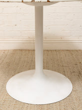 Load image into Gallery viewer, A white tulip pedestal table base on a woven jute rug against a white painted brick wall.
