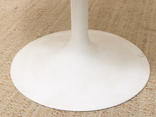 Load image into Gallery viewer, Close-up of a white tulip-style table base on a textured beige woven rug.

