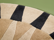 Load image into Gallery viewer, A close-up of a textured area rug with a geometric fan pattern in beige, tan, and black, set against a solid green background.
