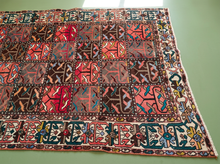 Load image into Gallery viewer, A square Persian-style wool rug with a complex multicolor geometric pattern, laid flat on a light green surface.
