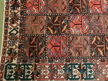 Load image into Gallery viewer, A close-up of a patterned area rug showing a grid of geometric and tribal-style panels in rust red, brown, cream, teal, and black, with a decorative border.
