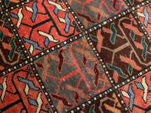 Load image into Gallery viewer, A close-up of a patterned rug with geometric panels in red, brown, gray, black, blue, and cream.
