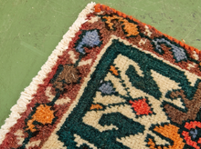 Load image into Gallery viewer, A close-up of a handwoven rug corner showing its intricate pattern and fringe, laid on a textured green floor.
