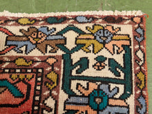 Load image into Gallery viewer, A close-up of a traditional patterned rug with cream, red, green, blue, and yellow geometric and floral motifs, laid flat on a green surface.
