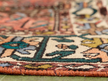 Load image into Gallery viewer, Close-up of a patterned area rug with a thick orange-pink fringed edge, featuring cream, teal, mustard, and brown woven motifs.
