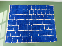 Load image into Gallery viewer, A rectangular blue shag rug with a white border and a brick-like block pattern, laid flat on a green background.
