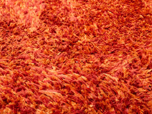 Load image into Gallery viewer, A close-up of a shaggy, high-pile rug in a warm blend of red, orange, and pink tones.
