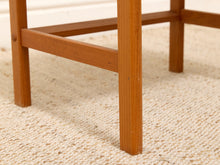 Load image into Gallery viewer, Close-up of a wooden table leg and footrest on a textured beige woven rug.
