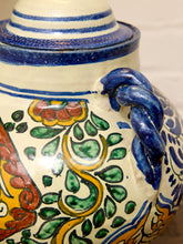 Load image into Gallery viewer, Close-up of a hand-painted ceramic jar with a blue glazed handle and lid, featuring traditional Mediterranean-style floral patterns in green, yellow, orange, and blue on a cream background.
