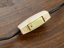 Load image into Gallery viewer, A close-up of a vintage cream-colored plastic switch with a yellow-green button, mounted on a black cord over a dark wood surface.
