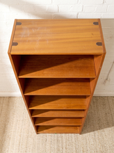 Load image into Gallery viewer, A mid-century modern wooden bookcase with five open shelves, made of warm medium-brown wood with dark metal corner brackets, set against a white brick wall and light beige rug.
