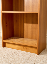 Load image into Gallery viewer, A close-up of a wooden bookshelf with two open shelves, showing a warm medium-brown wood grain finish, set against a light beige textured carpet.
