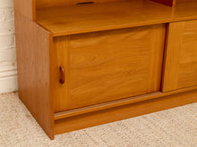 Load image into Gallery viewer, A close-up of a mid-century modern wooden cabinet with warm honey-toned wood grain, a single dark brown pull handle, and a cream-colored textured carpet underneath.
