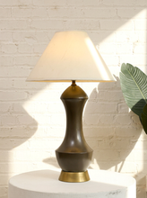 Load image into Gallery viewer, Vintage table lamp with tall sculptural charcoal-brown curving body, round brass-tone base, and oversized off-white tapered fabric shade
