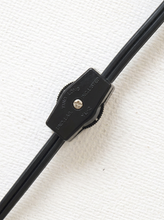 Load image into Gallery viewer, Close-up of a black adjustable lens clip on a black eyeglass arm, set against a textured white background.
