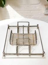 Load image into Gallery viewer, A vintage-style metal table organizer with a rectangular frame, wire basket-style center tray, and small side holders, displayed on a white table against a white brick wall background.
