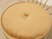 Load image into Gallery viewer, Close-up of a round tufted cushion in a warm camel beige fabric, showing the center button and part of the gold metal frame beneath.
