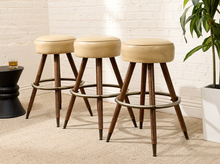 Load image into Gallery viewer, Set of three vintage bar stools with round cream upholstered seats, four splayed wood legs, and circular metal footrests
