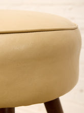 Load image into Gallery viewer, Close-up of a round upholstered stool seat in a warm beige or cream faux leather material, showing the side profile and a dark wooden leg against a light neutral background.
