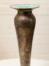 Load image into Gallery viewer, An antique-style metallic vase with a flared rim, featuring a mottled bronze and brown body with a turquoise patina on the interior, set against a light beige brick background.
