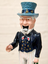 Load image into Gallery viewer, A hand-painted Uncle Sam figurine wearing a blue top hat with gold stars, a dark blue coat with red and white details, and white pinstriped trousers, shown against a light beige background.
