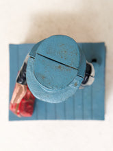 Load image into Gallery viewer, A top-down close-up of a toy soldier's helmet and shoulder area, featuring a distressed blue painted finish with rust-like speckling, set against a light beige background.

