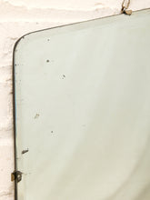 Load image into Gallery viewer, A vintage rectangular wall mirror with a dark metal frame and hanging loop, showing a light greenish tint and some scuffs, mounted on a white brick wall.
