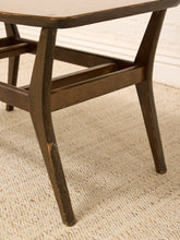 Load image into Gallery viewer, Close-up of a dark brown wooden table leg with a distressed finish, resting on a beige woven jute rug against a white paneled wall.
