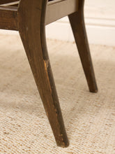 Load image into Gallery viewer, Close-up of a dark brown wooden chair leg with visible wear and scratches, resting on a textured beige woven rug.
