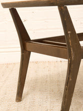 Load image into Gallery viewer, Close-up of the lower portion of a dark brown wooden chair, showing the curved backrest, legs, and slatted support beam, set against a white brick wall and light beige woven rug.
