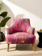 Load image into Gallery viewer, Modern accent chair with red, magenta, purple, pink, and yellow botanical-patterned upholstery, curved arms, and tapered wood legs
