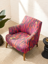 Load image into Gallery viewer, Modern accent chair with red, magenta, purple, pink, and yellow botanical-patterned upholstery, curved arms, and tapered wood legs
