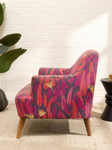 Load image into Gallery viewer, Modern accent chair with red, magenta, purple, pink, and yellow botanical-patterned upholstery, curved arms, and tapered wood legs
